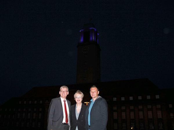Bürgermeister Kleebank und Gabriele Fliegel vom Wirtschaftshof mit Pal Dardei vor dem illuminierten Rathaus.