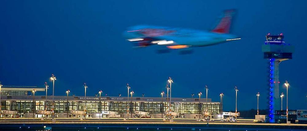 Ein Passagierflugzeug landet neben dem hell erleuchteten Berlin Brandenburg Airport Willy Brandt (BER) in Schönefeld (Brandenburg).