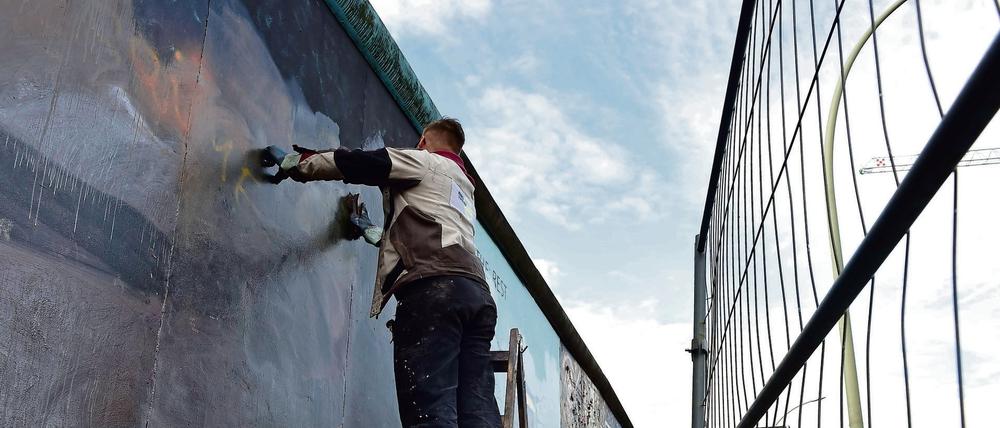 Ein Arbeiter entfernt hinter einem Bauzaun Graffitis von einem Bild auf der ehemaligen Berliner Mauer.