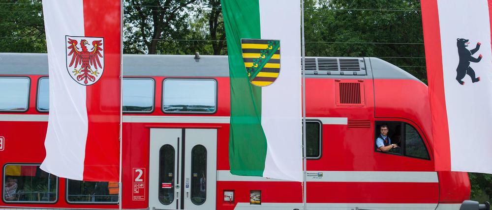Ein Regionalexpress der Deutschen Bahn fährt am 30.05.2016 in Baruth (Brandenburg) an den Landesfahnen von Brandenburg, Sachsen und Berlin vorbei. 