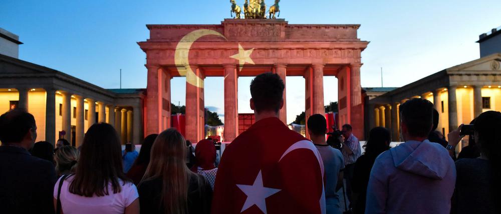 Die Menschen stehen zusammen vor dem Brandenburger Tor, an das die Flagge der Türkei gestrahlt wird.