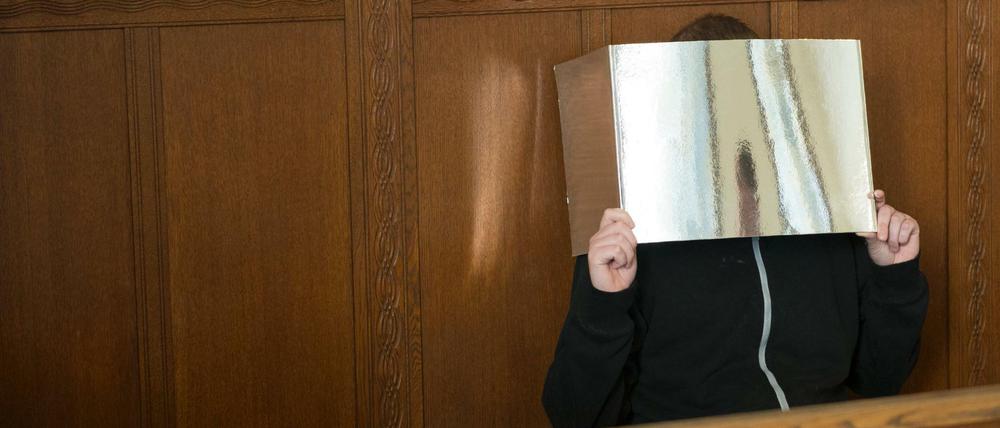 Der wegen Brandstiftung angeklagte Florian M. hält zum Prozessauftakt im Kriminalgericht Moabit in Berlin eine Pappe vor sein Gesicht. 