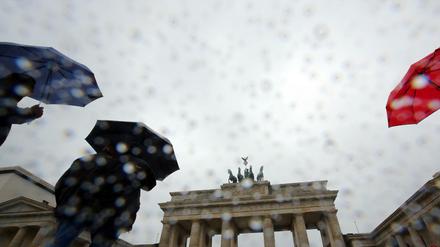 Bei Regen gehen Touristen vor dem Brandenburger Tor in Berlin vorbei. 