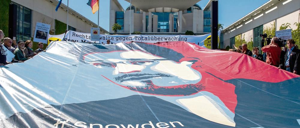 Ein Transparent mit dem Bild von Edward Snowden ist am 30.05.2015 in Berlin bei der Demonstration gegen Massenüberwachung durch Geheimdienste vor dem Bundeskanzleramt gespannt. Aufgerufen hat die Initiative «Rechtsanwälte gegen Totalüberwachung». Anlass ist der zweite Jahrestag der Enthüllungen von Edward Snowden. Foto: Paul Zinken/dpa +++(c) dpa - Bildfunk+++
