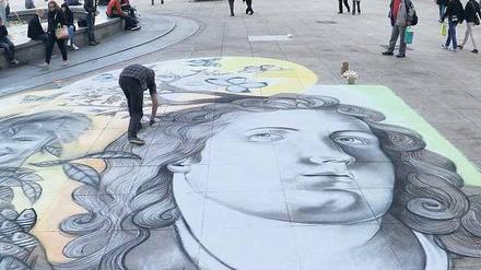 Das Ende der Regenzeit. Dieser Straßenmaler auf dem Alexanderplatz muss sich in den nächsten Tagen nicht sorgen, dass Regen seine Kunst wegspülen könnte. Es soll trocken bleiben. Foto: Paul Zinken/dpa
