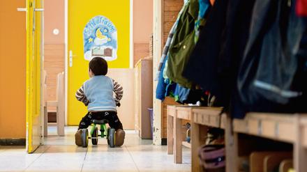 Ein Junge fährt in einer Kindertagesstätte mit einem Pukylino an einem Garderobenständer vorbei. 