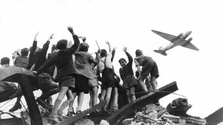 West-Berliner Jungen, die auf einem Trümmerberg stehen, winken einem US-Transportflugzeug zu (Aufnahme von 1948). 
