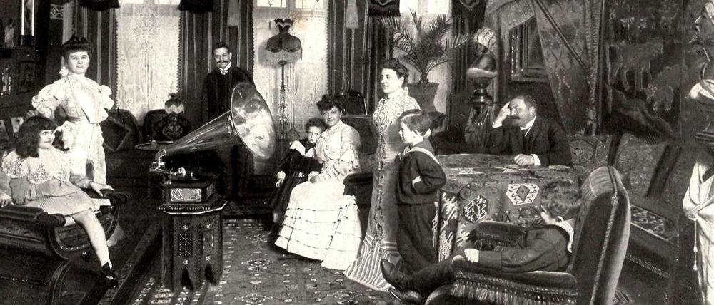 In einem gediegen eingerichteten Wohnzimmer der Jahrhundertwende hat sich eine wohlhabende Berliner Familie um ein Grammophon versammelt.