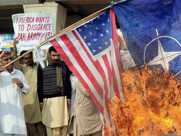 Wütende Menschen verbrennen die USA- und die Nato-Fahne auf der Straße in der pakistanischen Stadt Multan.