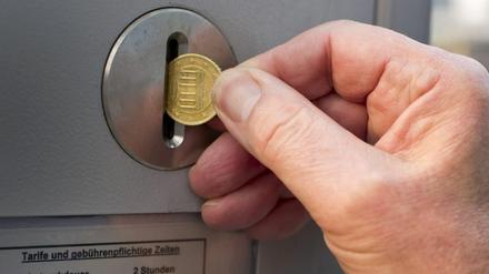 Hand wirft Kleingeld in Schlitz eines Parkautomaten.