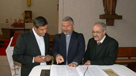 SPD-Fraktionschef Raed Saled beugt sich mit Abuna Murat Üzel und Amill Gorgis von der Syrisch-Orthodoxen Kirche über aramäische Gebetsbücher.