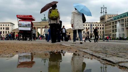 Passanten schützen sich am Brandenburger Tor mit Schirmen vor dem Regenwetter.
