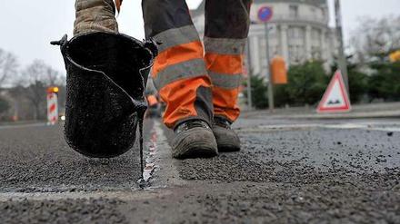 Straßenbild: Ein Bauarbeiter bessert Rillen und Löcher im Belag aus.