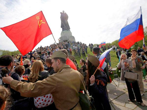 Menschen in militärischen Uniformen schwenken russische und sowjietische Flaggen im Treptower Park.
