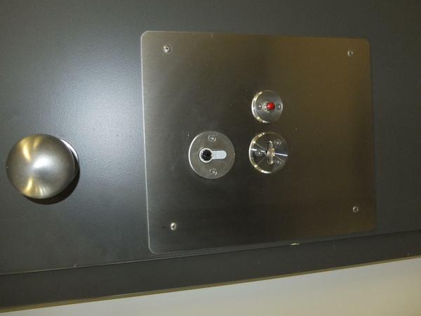 Die Tür von außen. Das große Schlüsselloch ist für die Aufpasser. Mit einem kleinen Schlüssel können die Verwahrten ihre Zelle abschließen, wenn sie auf dem Sportplatz oder bei der Arbeit sind. Die Stellung des roten Knopfs zeigt an, ob die Tür verriegelt ist. 