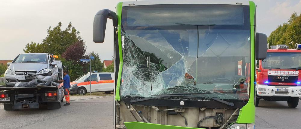 Ein Schulbus steht nach einem Unfall beschädigt auf der Straße, während ein Fahrzeug abgeschleppt wird. 