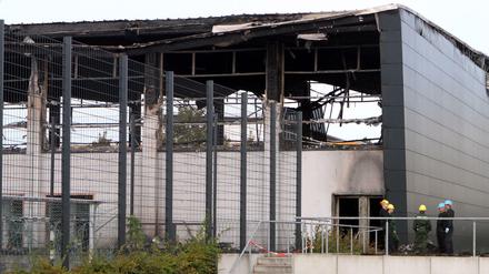Aufgebrochen und angezündet: Die abgebrannte Halle in Nauen, rechts davor die Ermittler der Polizei.