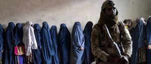 Ein Taliban-Kämpfer steht Wache, während Frauen darauf warten, von einer humanitären Hilfsorganisation verteilte Lebensmittelrationen zu erhalten.