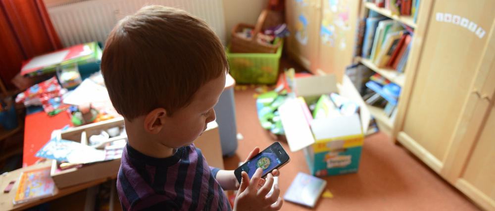 Ein Junge spielt in seinem Kinderzimmer auf einem Smartphone ein Computerspiel.
