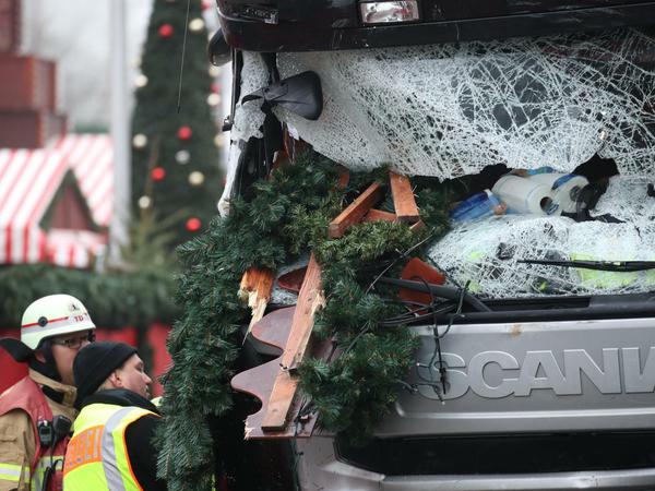 Ein Polizist und ein Feuerwehrmann stehen nach dem Anschlag auf den Weihnachtsmarkt am Breitscheidplatz vor dem beschädigten Tatfahrzeug.