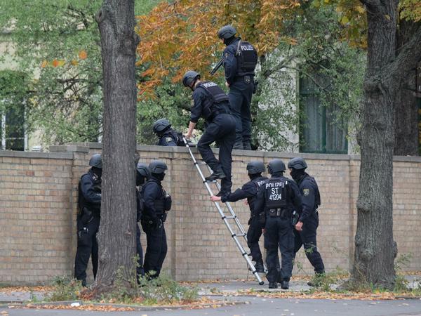 Polizisten mit Schutzhelmen übersteigen in Halle eine Mauer. 