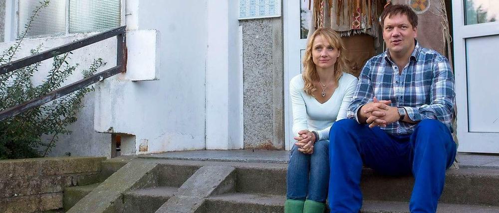 Charly Hübner und Christina Große sitzen vor dem Eingang eines Plattenbau-Wohnblocks in Schwerin. 