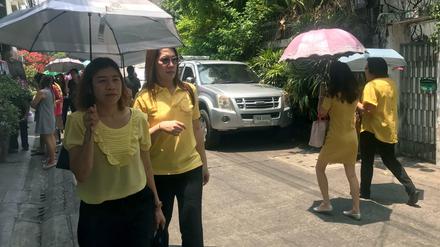 Passanten sind in gelber Kleidung auf einer Straße in Thailands Hauptstadt Bangkok unterwegs.