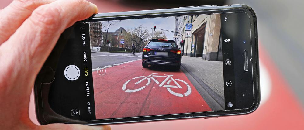  Auf einem Smartphone ist das Bild eines Autos zu sehen, das auf einem Radfahrstreifen hält. (Symbolbild)