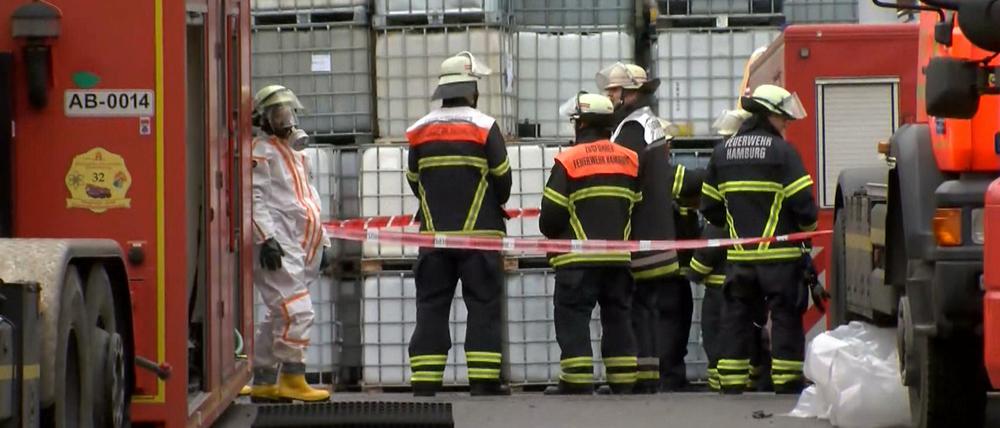 Einsatzkräfte der Feuerwehr stehen in Schutzanzügen vor einer Lagerhalle im Hamburger Stadtteil Steinwerder.