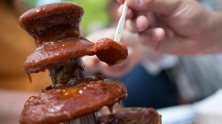 Ein Besucher tunkt am Sonntag bei der Deutschen Grill- und BBQ-Meisterschaft in Hennef (Nordrhein-Westfalen) ein Stück Wurst in einen Brunnen mit Currysoße. Ingesamt brutzelten rund 40 Teams um den Titel.