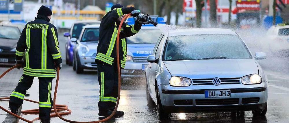 Feuerwehrmänner reinigen am Sonntag in Duisburg (Nordrhein-Westfalen) Autos. Eine Rauchwolke mit Asbeststaub ist nach einem Brand in einer Lagerhalle über die Stadt gezogen.