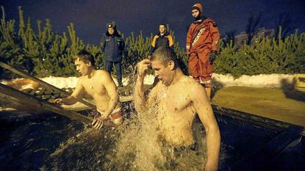 Ein Russe wäscht sich im Eisbad frei von Sünden. Polizei und Rettungsteams stehen bereit.