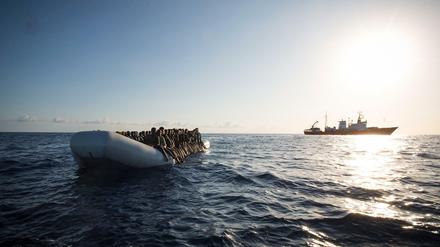 Ein Flüchtlingsboot auf dem Mittelmeer und im Hintergrund ein Schiff der Hilfsorganisation SOS Mediterranee.