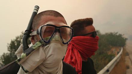 Zwei Männer schützen sich nahe dem Ferienort Kineta mit Tüchern und einem Schnorchel vor dem Rauch eines Großbrandes.