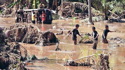 Katastrophengebiet Mindanao. Bewohner waten durch den Schlamm, den die Sturzflut hinterlassen hat. Fotos: dpa(2)