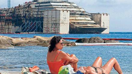 Hoch aufgerichtet präsentiert sich die Costa Concordia, während Strandbesucher den Tag genießen.