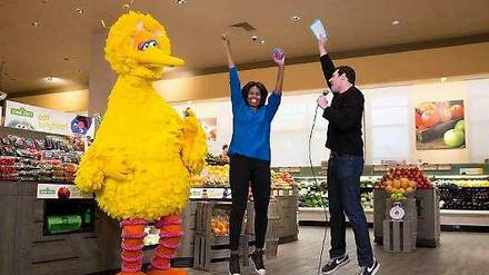 Michelle Obama (m) mit "Bibo", dem gelben Vogel aus der Kindersendung "Sesamstraße", und dem Moderator der US-Sendung "Funny or Die" im Supermarkt.