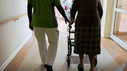 Beine einer Pflegerin und einer alten Frau mit Rollator von hinten auf einem langen Flur