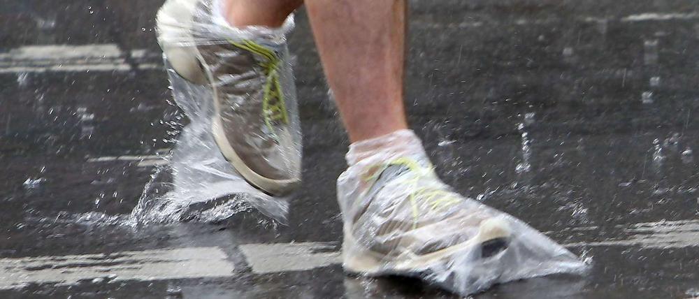 Regen in Berlin, Plastiktüten an den Füßen: Hier schützt sich ein Passant vor der Nässe. 