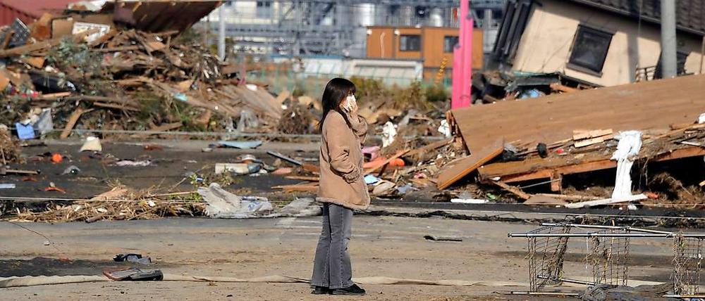 Eine Frau steht vor zerstörten Gebäuden in Soma, Fukushima.