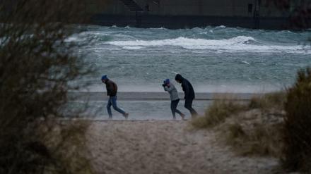 Spaziergänger stemmen sich gegen Windböen vor dem vom Wind aufgepeitschten Wasser am Ostsee-Strand.