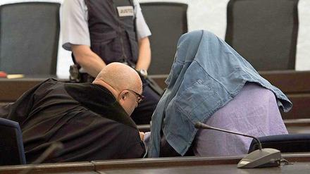 Der Angeklagte im Koffermord-Prozess, der eine Jacke über dem Kopf trägt, spricht am Dienstag in Stuttgart mit seinem Anwalt.