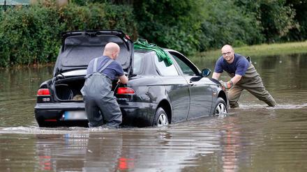 Feuerwehrleute in Offenbach bergen am ein Auto, das nach Starkregen auf einer überschwemmten Straße liegen geblieben war.