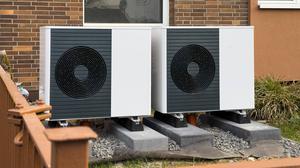 Zwei Wärmepumpen werden an einem Mehrfamilienhaus in einem Vorgarten montiert.