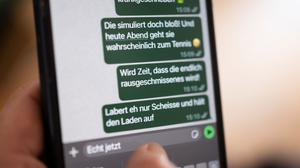 Eine Person hält ein Smartphone in der Hand, auf dessen Bildschirm beleidigende Nachrichten in einem Chat zu sehen sind (gestellte Szene).