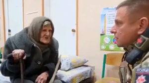 Eine 98-jährige ukrainische Frau sitzt auf einem Bett und spricht mit einem Mann in Uniform.