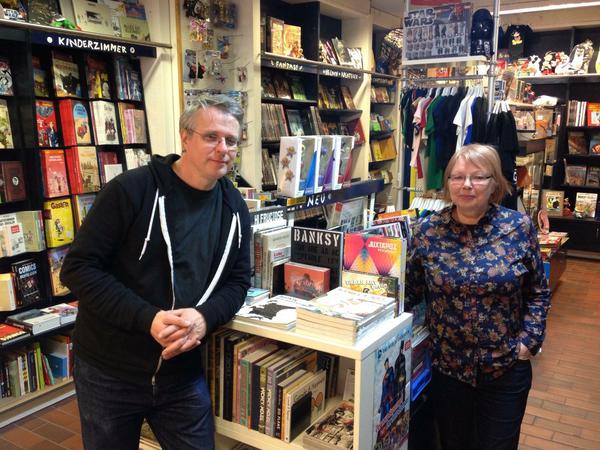 Die Besitzer des Comicladens Grober Unfug stehen zwischen den Bücherregalen.
