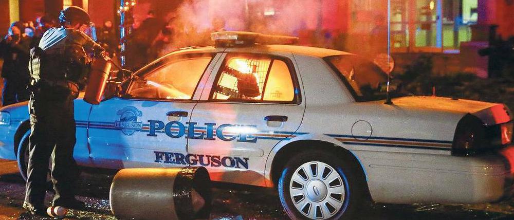 Brennende Wut. Ein Polizist versucht das Feuer zu löschen, das Protestierende in einem Polizeiauto in Ferguson gelegt haben.
