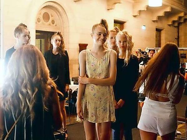 Ein lächelndes, junges Model steht im Nackstage-Chaos der Fashion Week herum