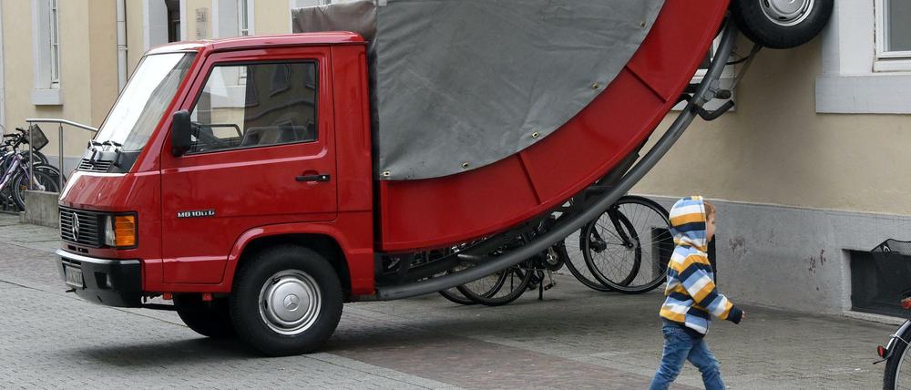 Der österreichische Künstler Erwin Wurm brachte das rote Fahrzeug an der Hauswand an. Da zwei Räder im Halteverbot standen, gab ein Polizist dem Wagen ein Knöllchen.